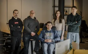 Vijf teamleden in het kantoor, enkelen met over elkaar geslagen armen en één zittend op een stoel, glimlachend