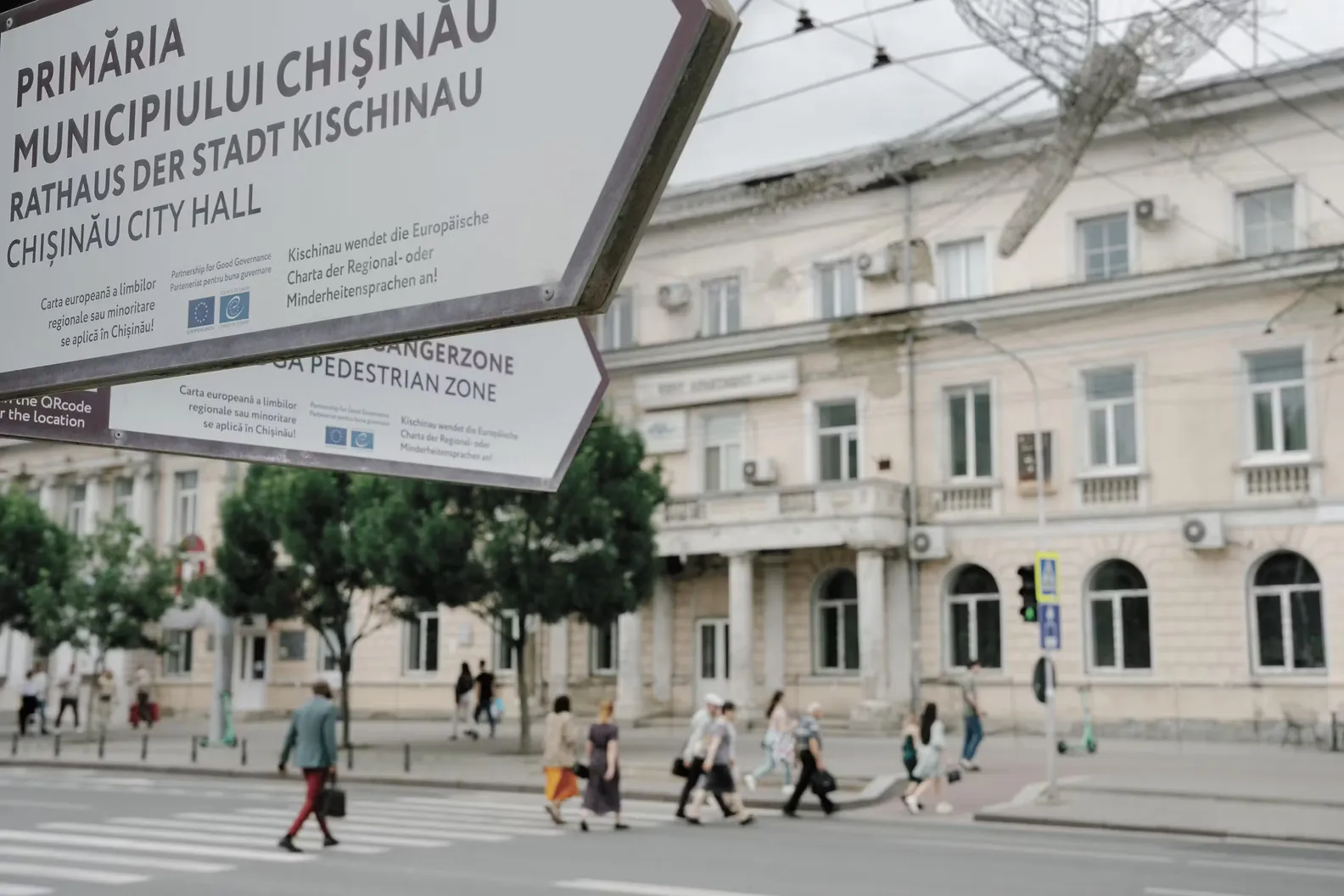 Een straatnaambord van het stadhuis van Chisinau op de voorgrond terwijl voetgangers de weg oversteken voor een gebouw in het centrum van Chisinau.